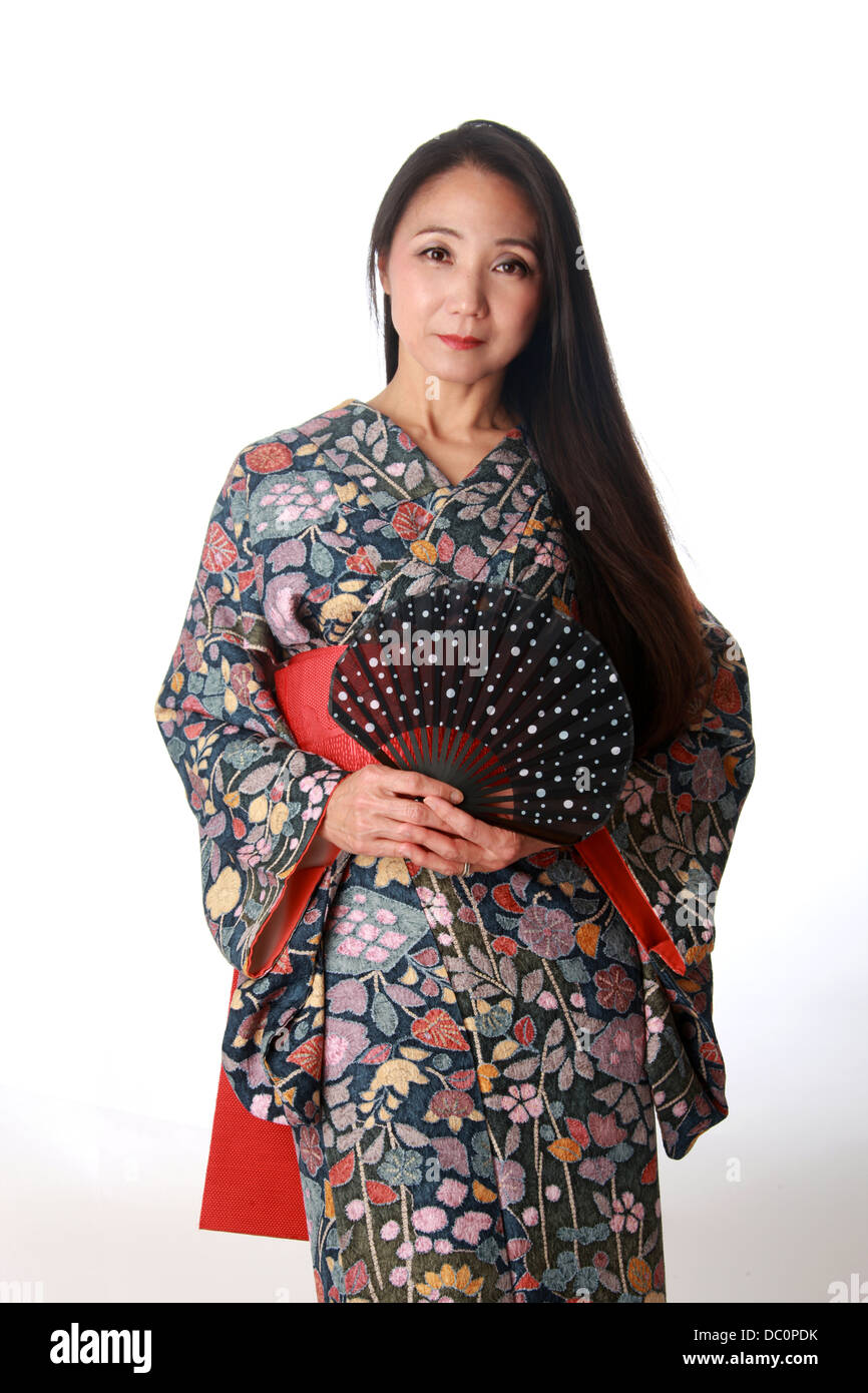 Japonais assis sur le plancher traditionnel portant un kimono à motifs bleu et rouge et la tenue d'un ventilateur Banque D'Images