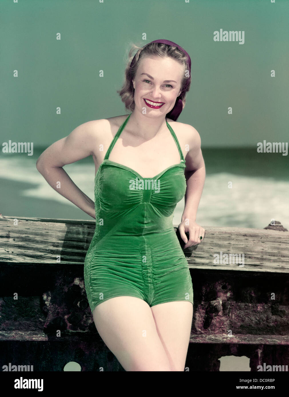 1940 YOUNG SMILING WOMAN WEARING GREEN VELVET MAILLOT DE POSING LEANING ON DIVING BOARD Banque D'Images