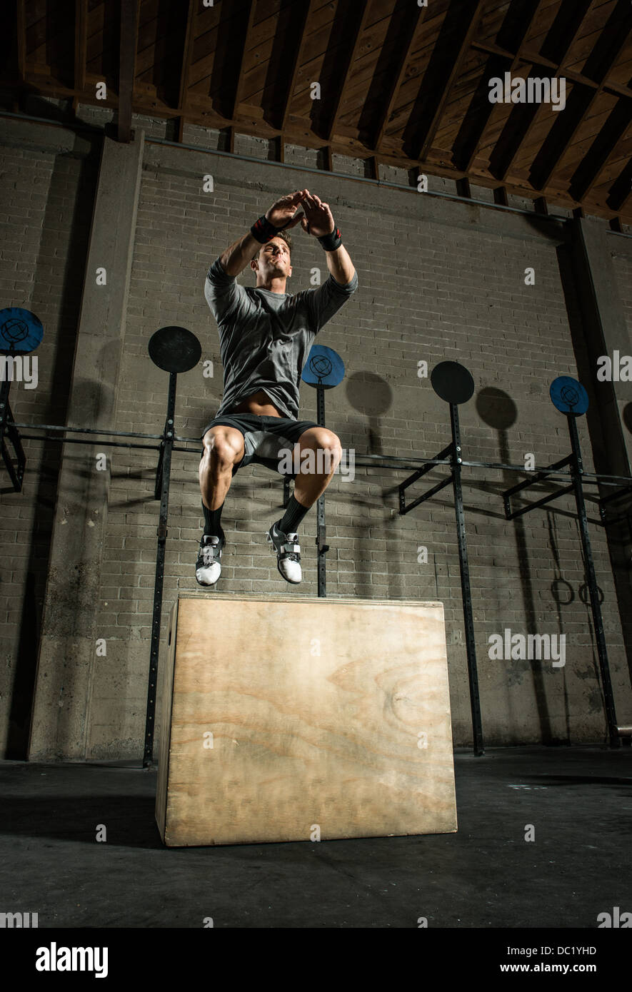 Jeune homme sautant d'un coffret en bois dans une salle de sport Banque D'Images