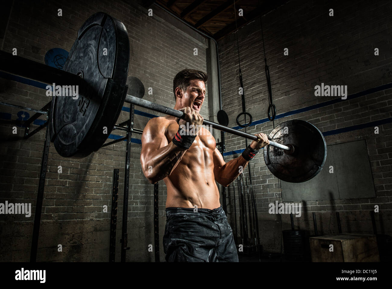 Jeune homme d'effectuer des biceps avec barbell in gym Banque D'Images