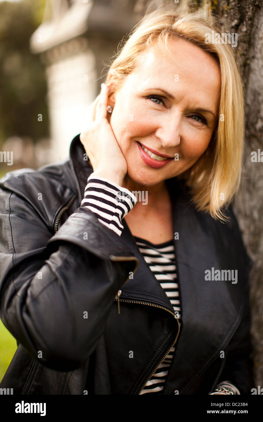 Young woman wearing leather jacket and smiling in park, portrait Photo ...