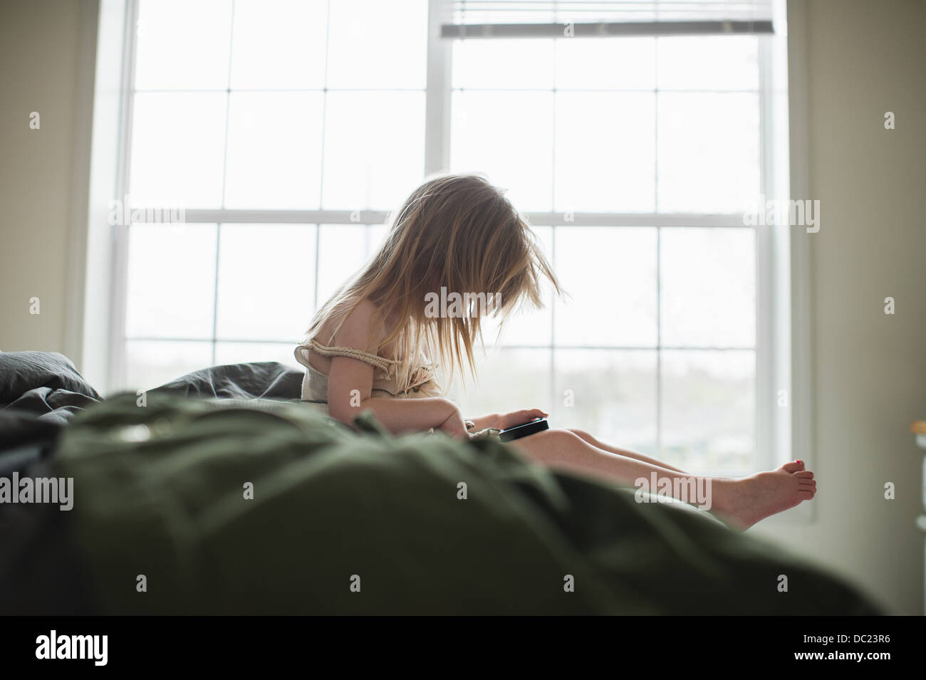 Girl sitting on bed using smartphone Banque D'Images