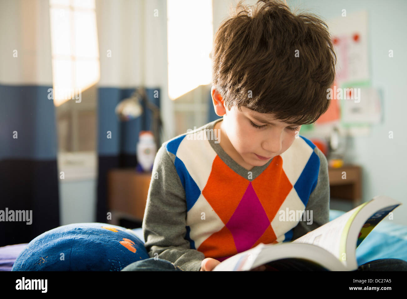 Boy sitting on bed reading book Banque D'Images