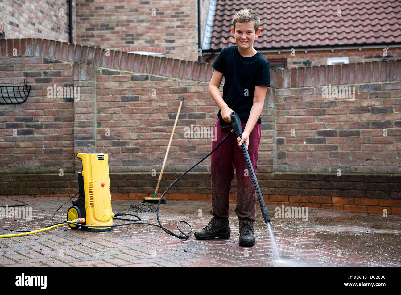 Un garçon de 13 ans utilise une rondelle de puissance pour nettoyer le bloc ouvrir dur à son domicile pour obtenir de l'argent de poche. Banque D'Images