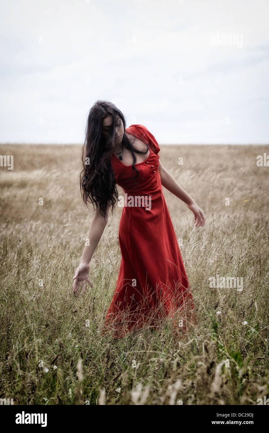 Une femme dans une robe rouge sur un champ, jouer avec le grain Banque D'Images