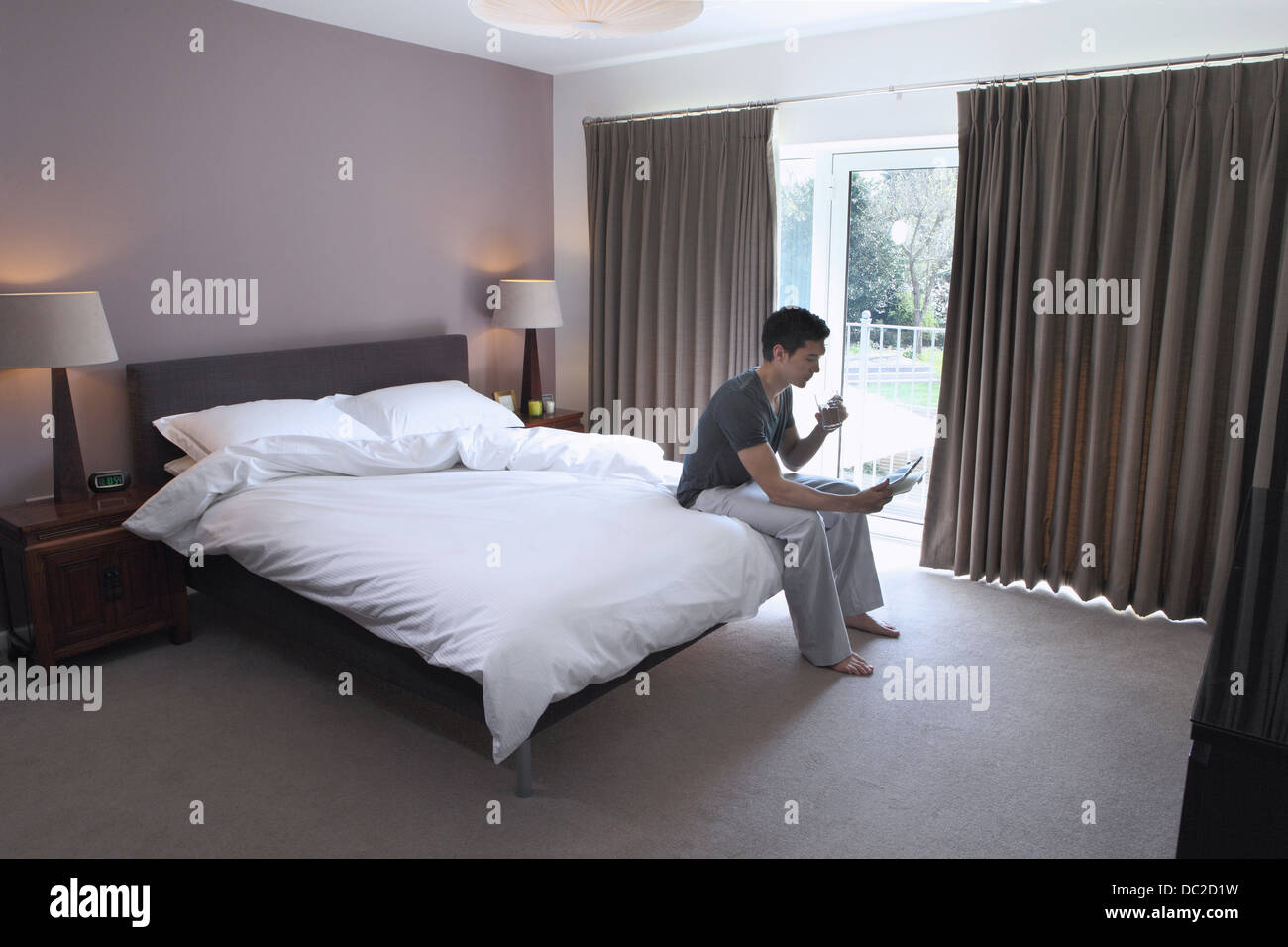 Man sitting on bed looking at digital tablet Banque D'Images