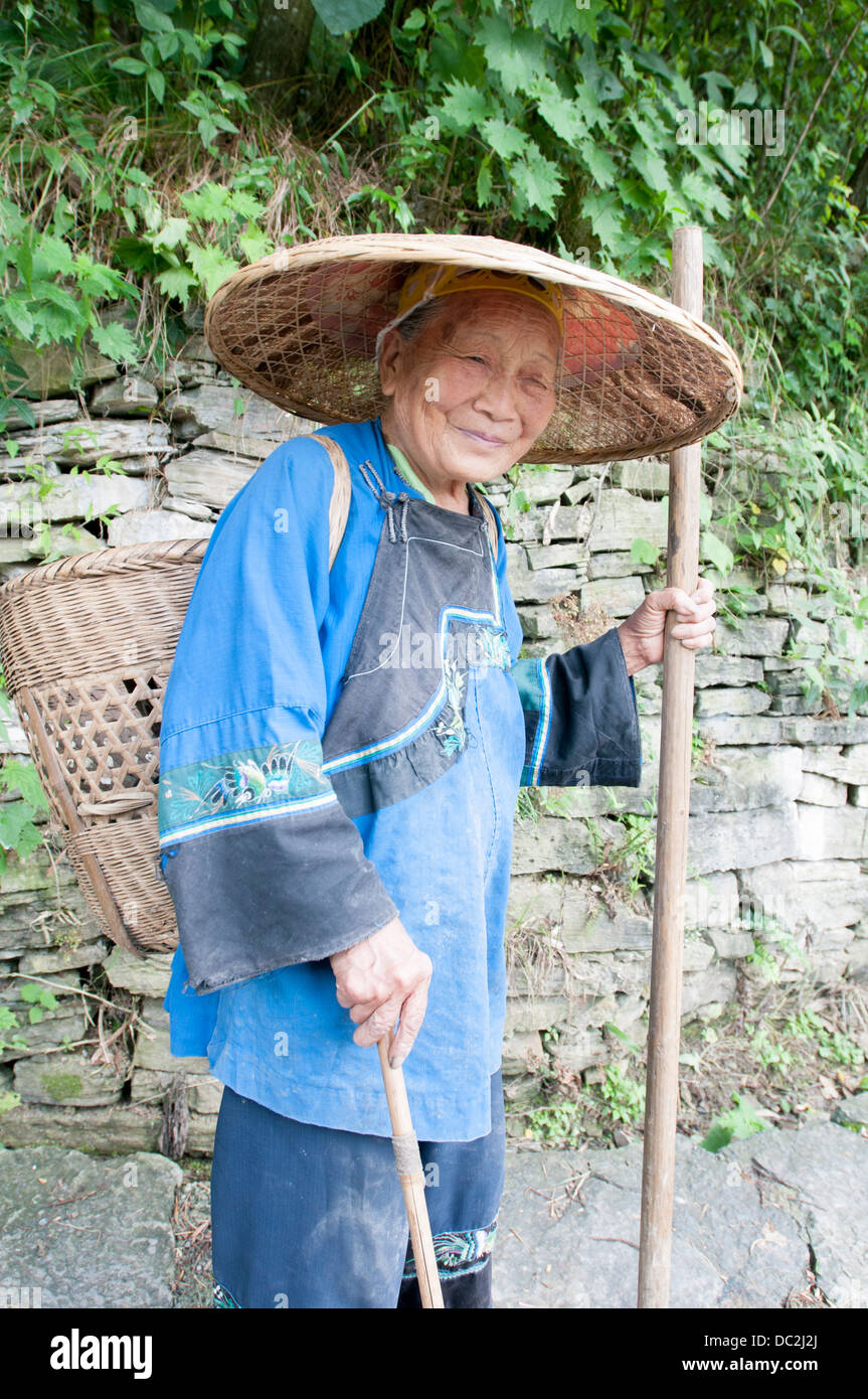 Une vieille femme robes ethniques Miao en bambou avec un panier sur son dos et double bâton dans ses mains. Banque D'Images