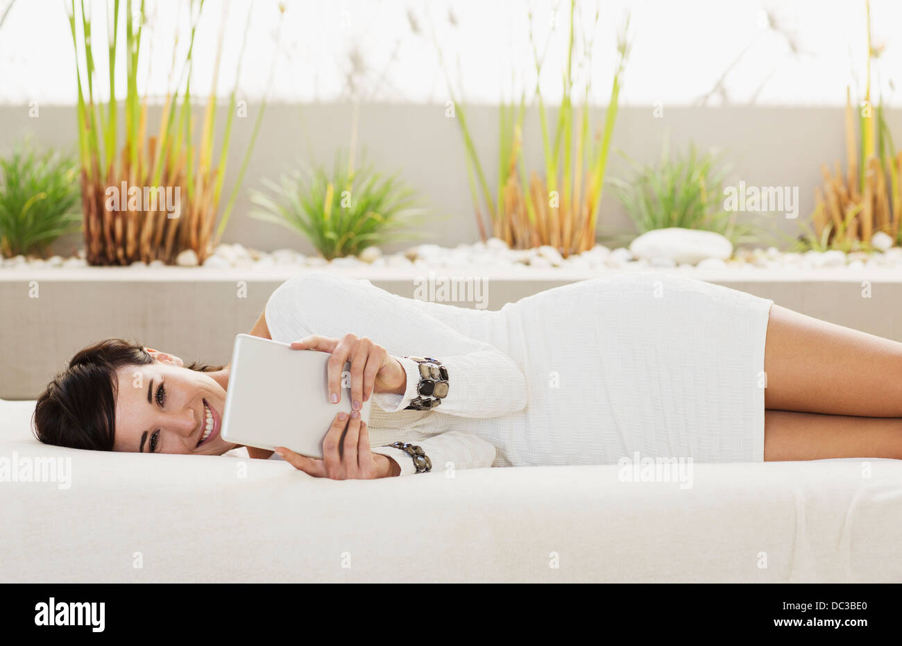 Portrait of smiling woman laying on sofa using digital tablet Banque D'Images