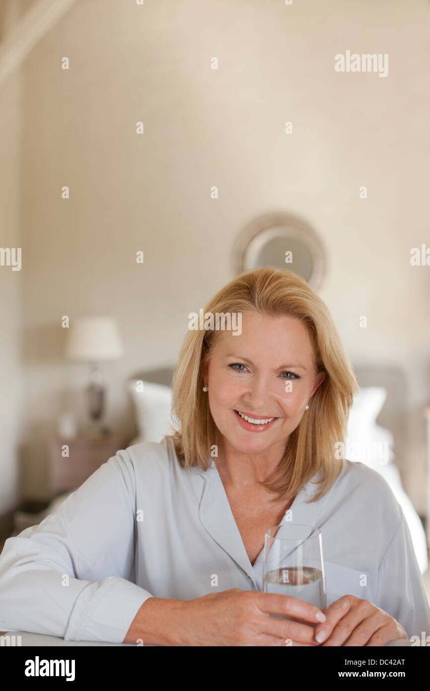 Portrait of smiling woman drinking glass of water dans la chambre Banque D'Images
