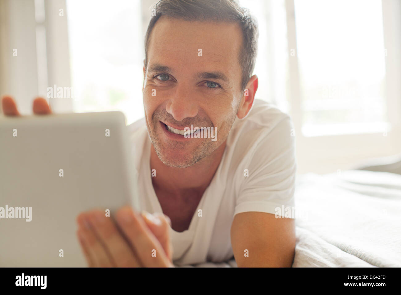Portrait of smiling man using digital tablet in bed Banque D'Images