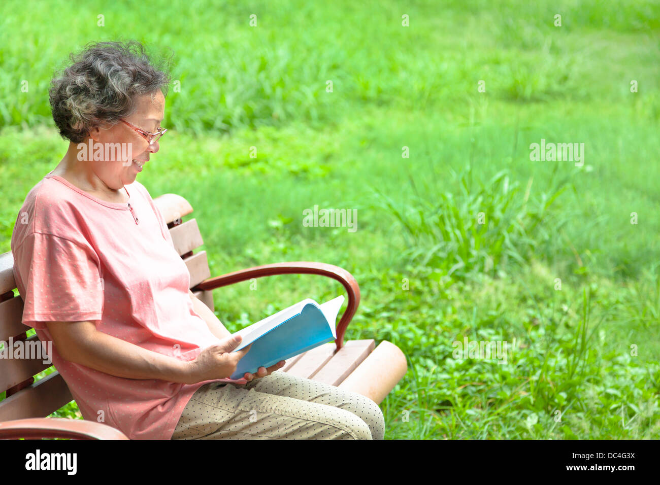 Happy senior femme assis sur un banc et la lecture d'un livre Banque D'Images