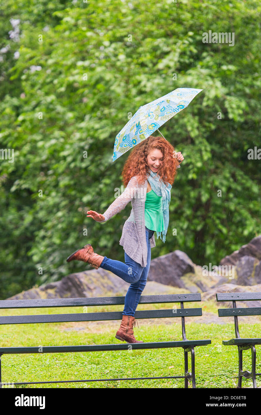 Femme avec parapluie danser sur un banc dans le parc Banque D'Images