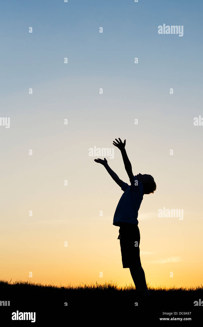 Garçon avec ses mains en l'air au coucher du soleil. Silhouette Banque D'Images