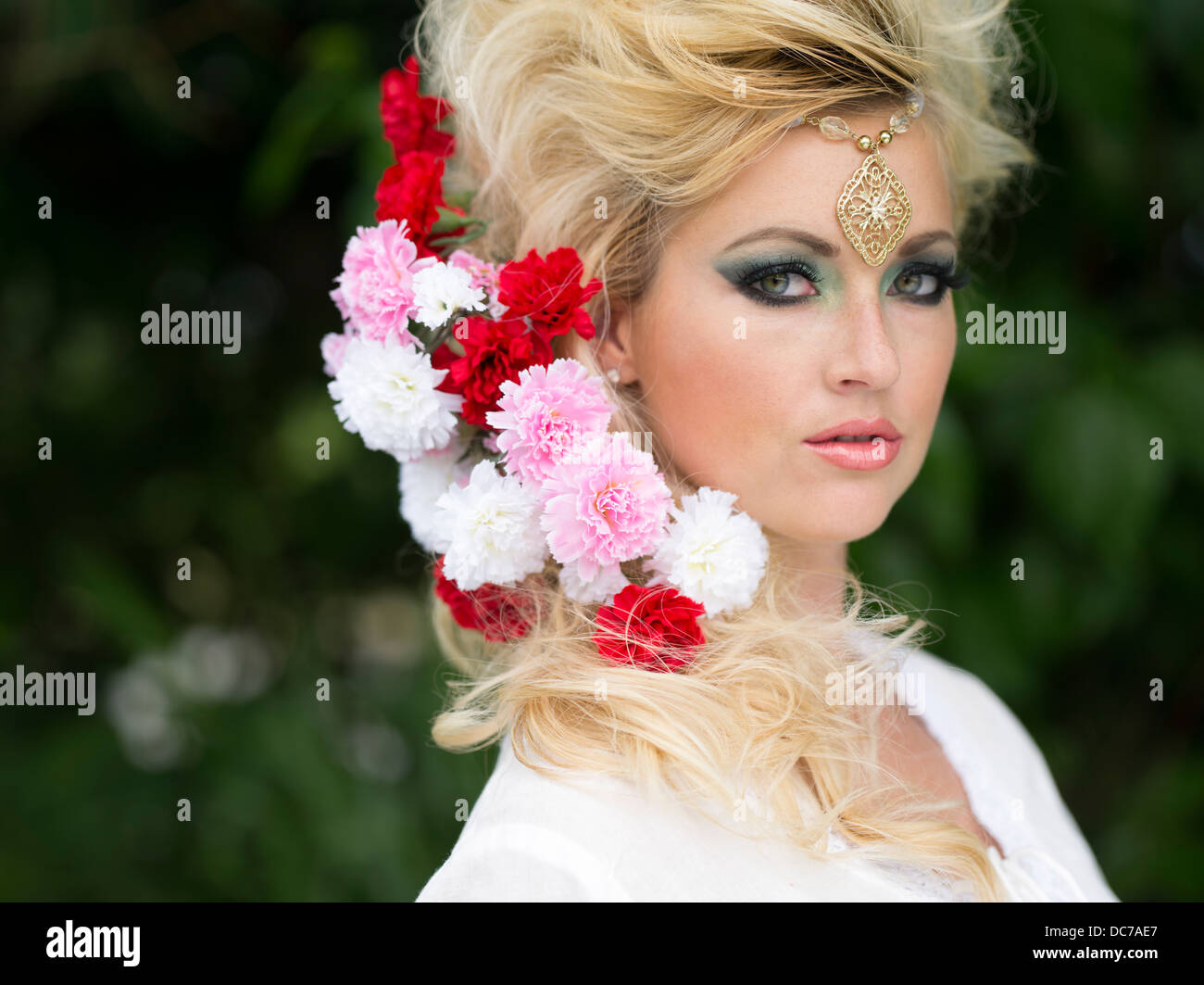 Belle blonde woman dans la vingtaine avec des fleurs dans les cheveux et des bijoux sur le front Banque D'Images