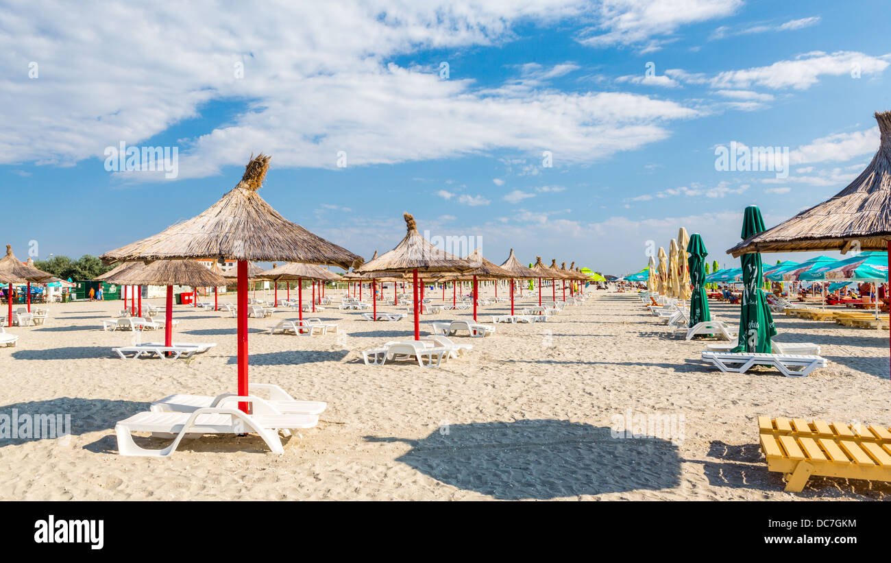 Rangée de paille et de parasols et chaises longues sur une plage de sable fin Banque D'Images