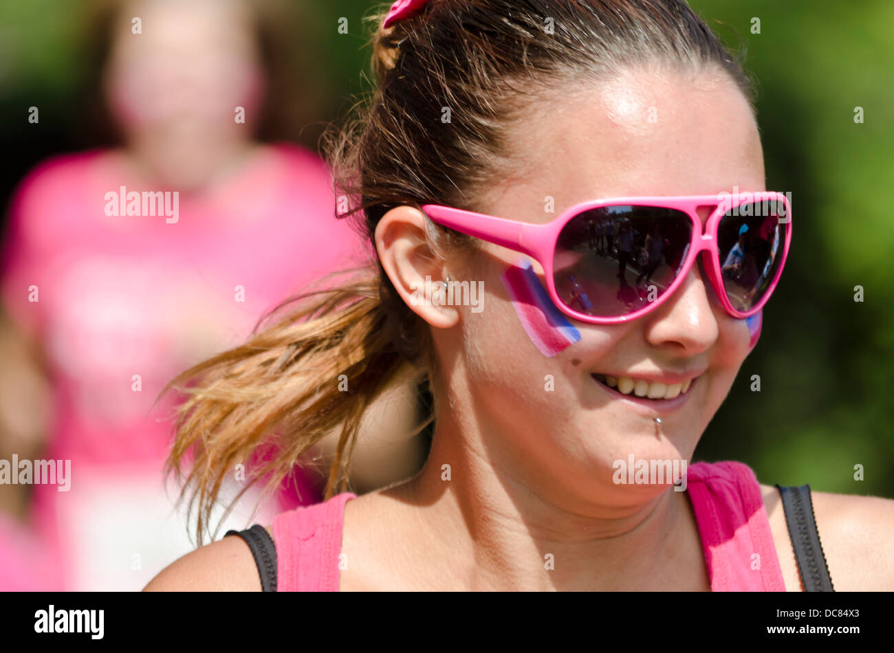 Jeune femme dans des lunettes de soleil roses courant dans l'événement annuel race for Life aidant à collecter des fonds pour la recherche sur le cancer au Royaume-Uni Banque D'Images