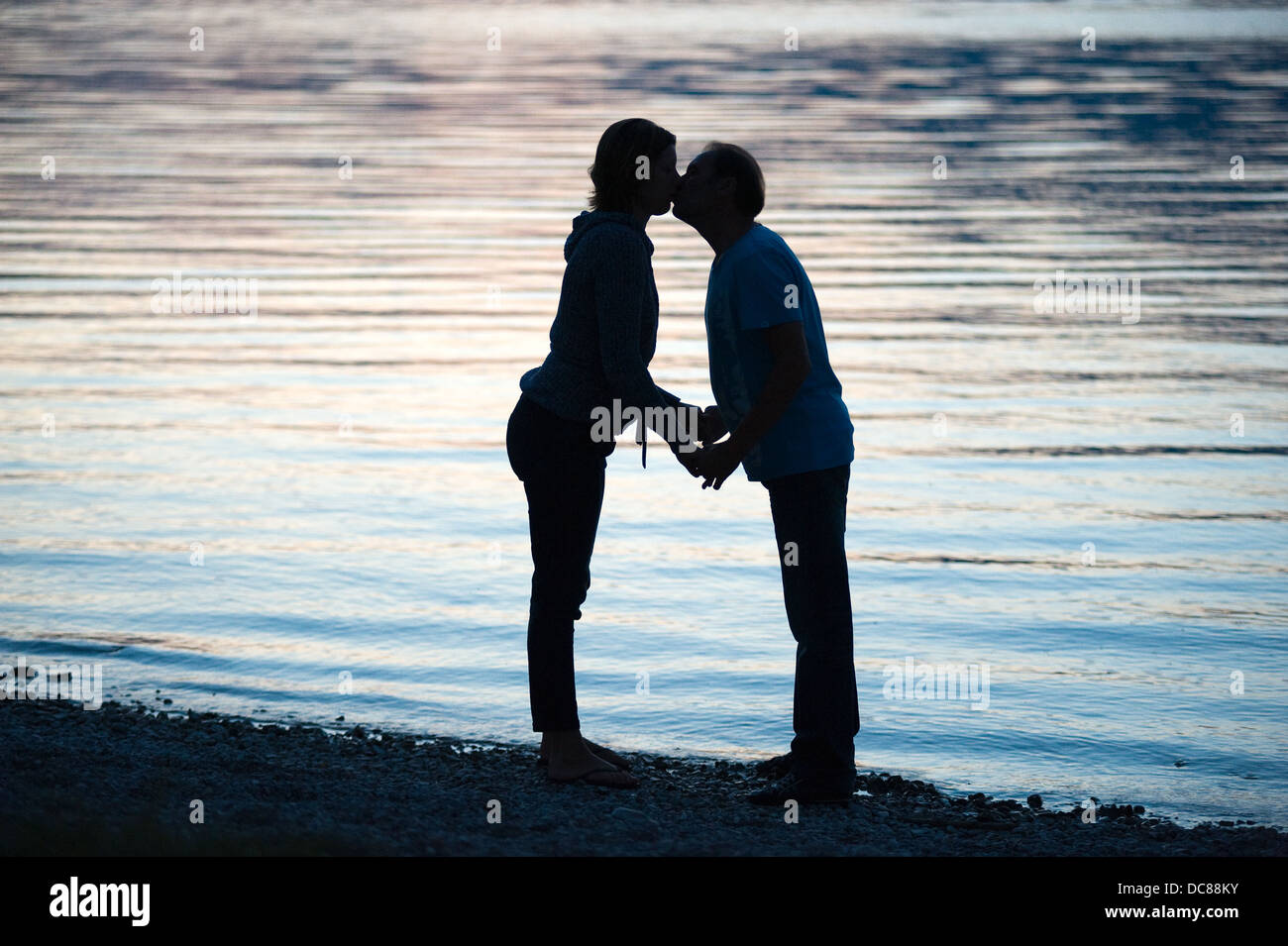 Un couple s'embrasser dans le crépuscule sur la plage d'un lac Banque D'Images