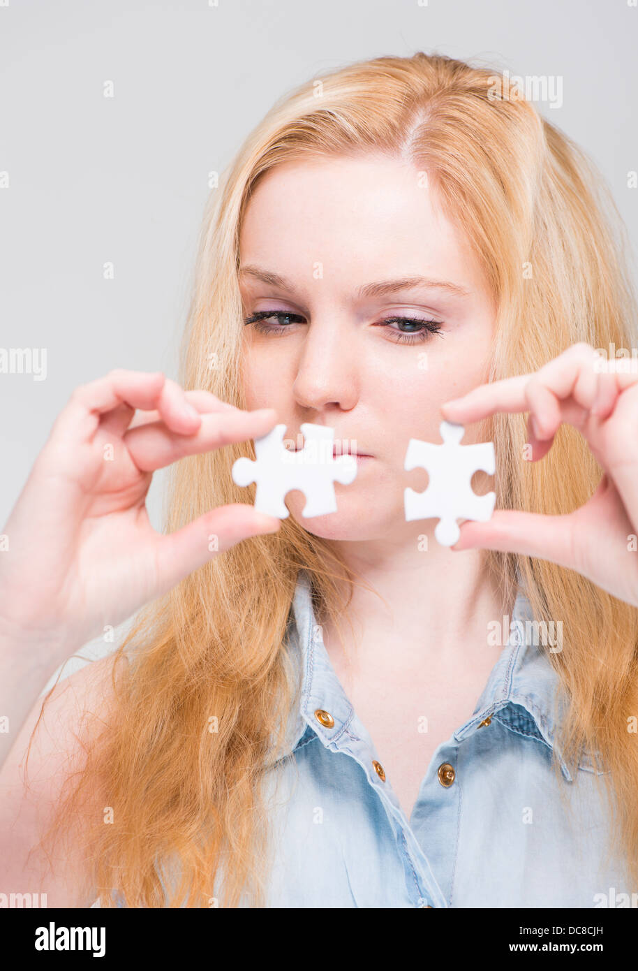 Jeune blond woman holding et l'examen de deux pièces de puzzle blanc Banque D'Images