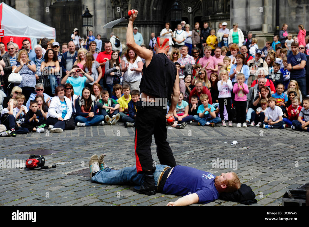 West Parliament Square, centre-ville d'Édimbourg, Écosse, Royaume-Uni, lundi 12 août 2013. Street Performer Mighty Gareth se préparant à jongler avec un couteau et des balles au-dessus d'un volontaire du public pendant le Festival International Fringe d'Édimbourg Banque D'Images