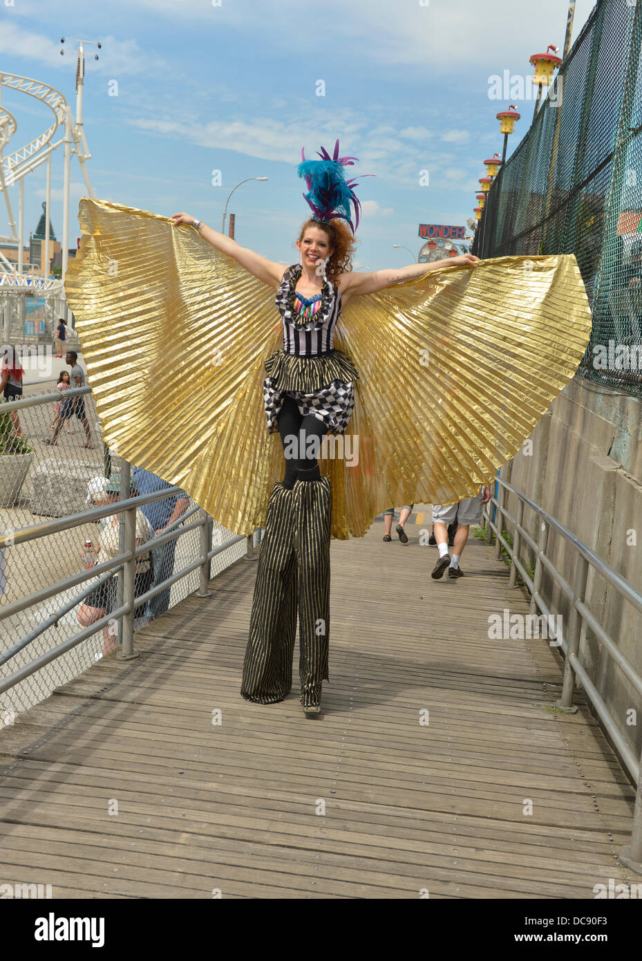 Brooklyn, New York, USA. 10 août 2013. À Coney Island, des Échasses KAE BURKE, Dame de cirque, porte une robe de soirée et costume cape d'or, haute comme elle marche sur pilotis sur la célèbre promenade. Banque D'Images