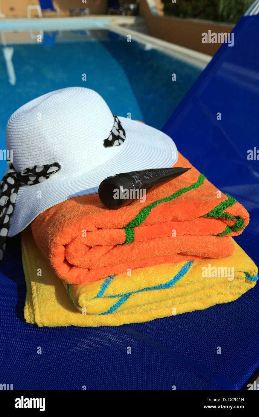 Les serviettes de plage, chapeau de soleil et crème solaire sur un transat au bord de la piscine Banque D'Images