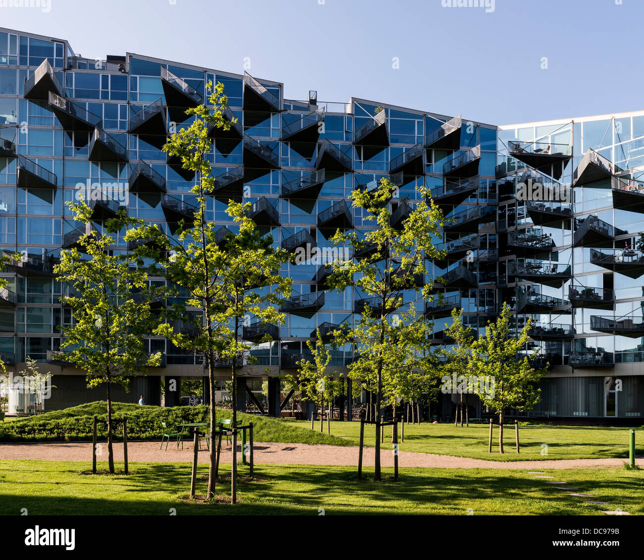Maisons VM, Copenhague, Danemark. Architecte : intrigue, 2013. Vue sur le bâtiment d'arbres et d'herbe en premier plan. Banque D'Images