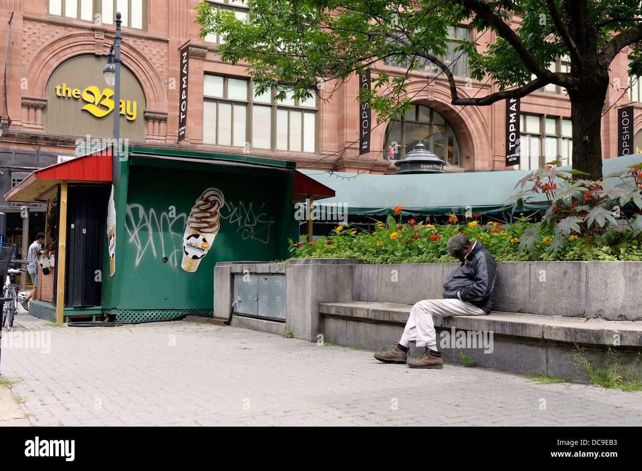 Sans-abri assis endormi sur un banc de béton au centre-ville de Montréal. Banque D'Images