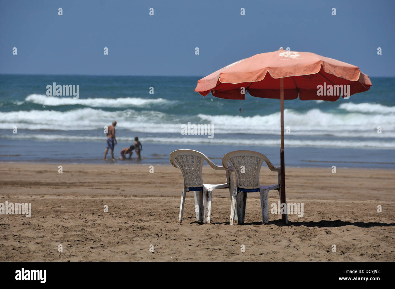Parasol et deux chaises longues à la plage de Casablanca, Maroc avec vue sur la mer et les gens à l'arrière-plan flou Banque D'Images