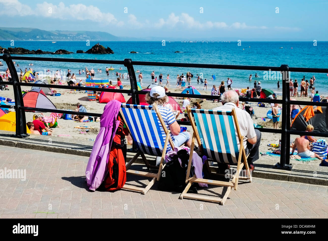 En Looe Cornwall - Les vacanciers assis dans des chaises longues donnant sur une longue plage de Looe est bondé et Cornwall UK Banque D'Images