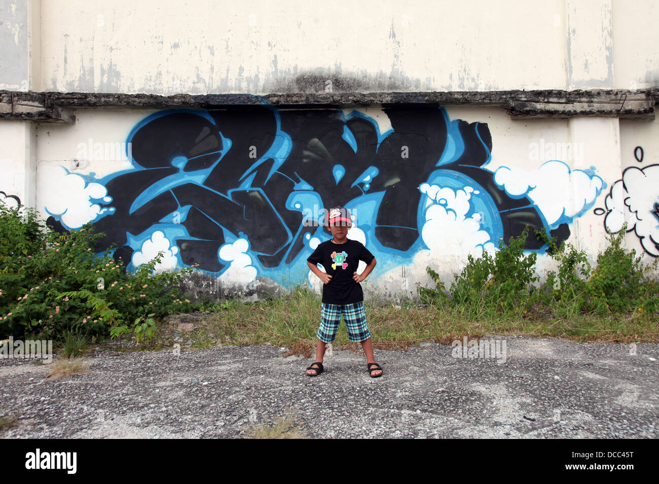 C'est une photo d'un graffiti tag bleu sur un mur sur un no man's land area en Malaisie. Nous voyons l'herbe et détruit un mur poussiéreux sale Banque D'Images