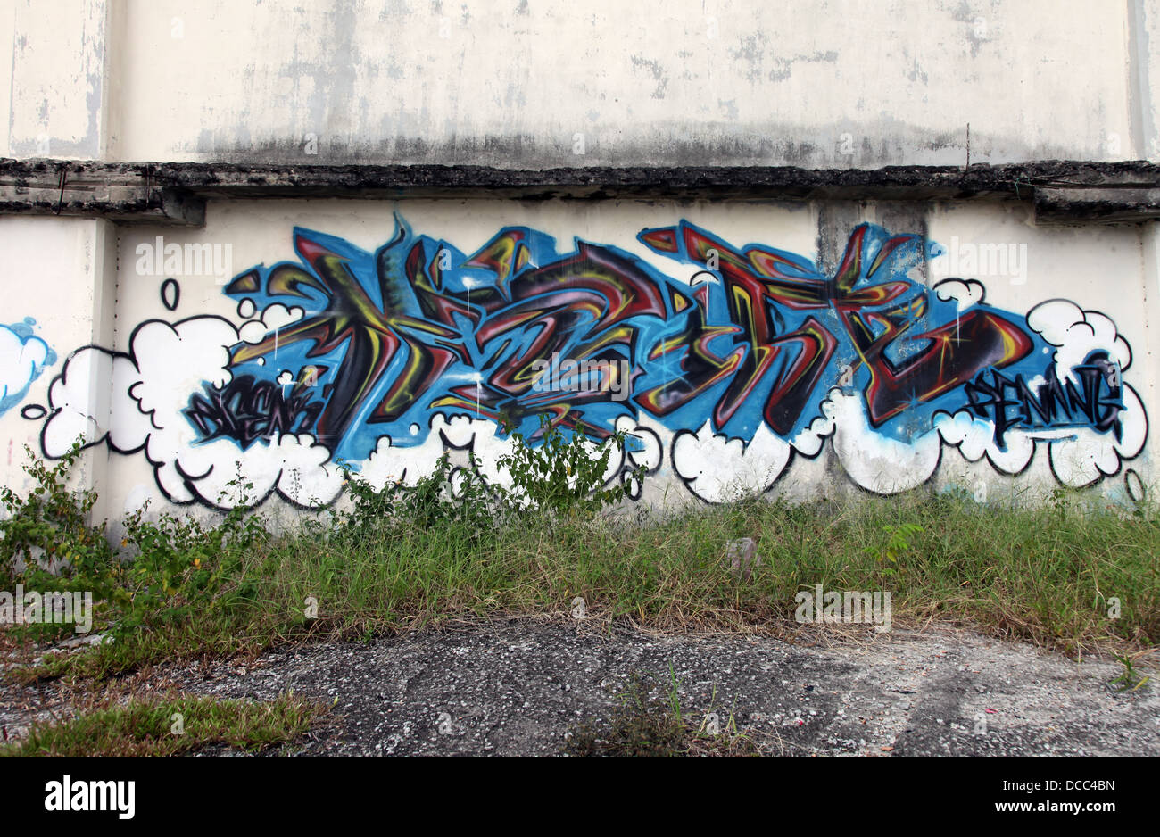 C'est une photo d'un graffiti tag bleu sur un mur sur un no man's land area en Malaisie. Nous voyons l'herbe et détruit un mur poussiéreux sale Banque D'Images