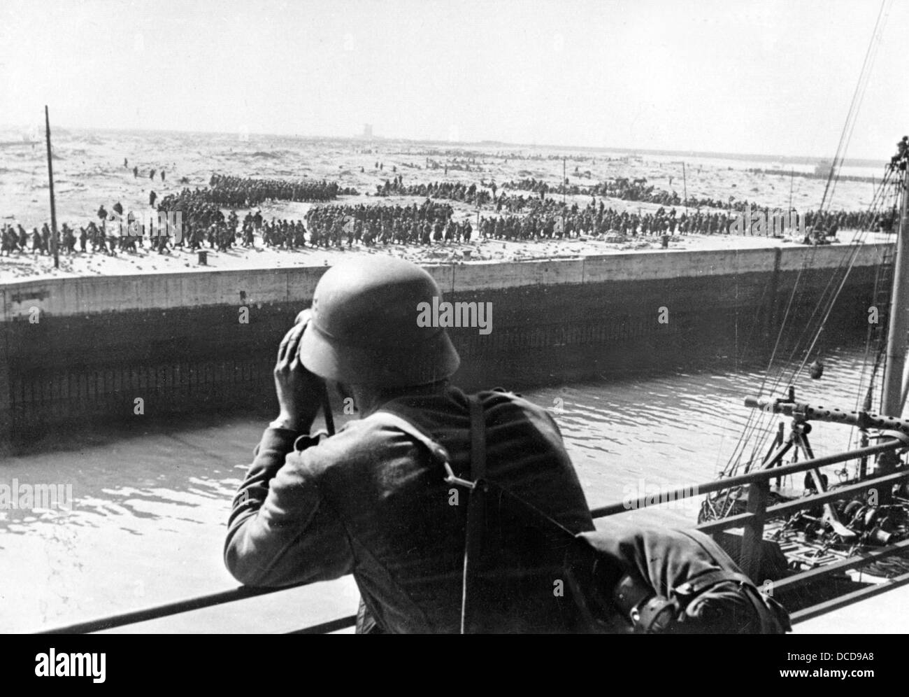 Un membre de la Wehrmacht allemande regarde à travers une paire de jumelles sur des prisonniers de guerre français et britanniques dans le port de Dunkerque sur le front occidental en France en juin 1940. Fotoarchiv für Zeitgeschichte Banque D'Images