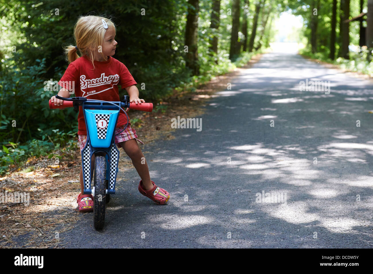 L'équilibre de l'enfant blond girl riding Bike in forest road, l'été Banque D'Images