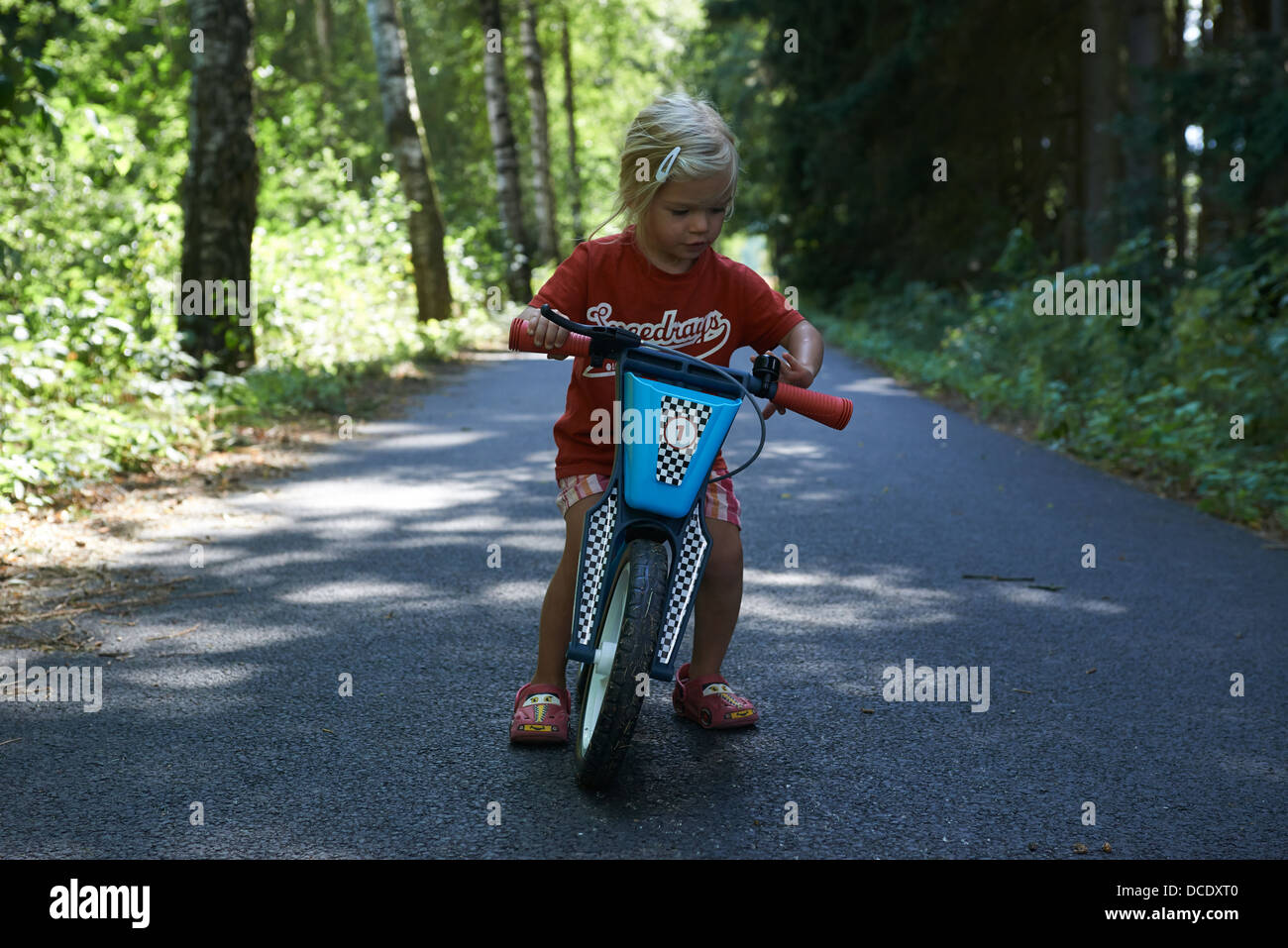 L'équilibre de l'enfant blond girl riding Bike in forest road, l'été Banque D'Images