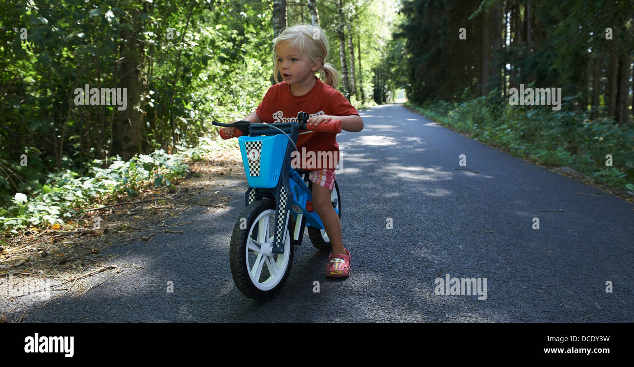 L'équilibre de l'enfant blond girl riding Bike in forest road, l'été Banque D'Images