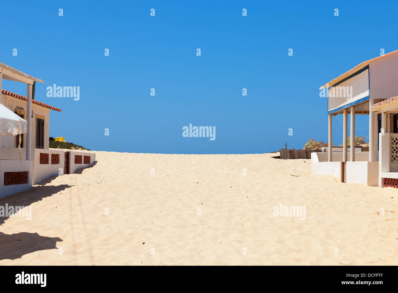 Golden Beach sand empiéter sur les bâtiments en bord de mer sur la côte ensoleillée sous un ciel d'été bleu clair Banque D'Images
