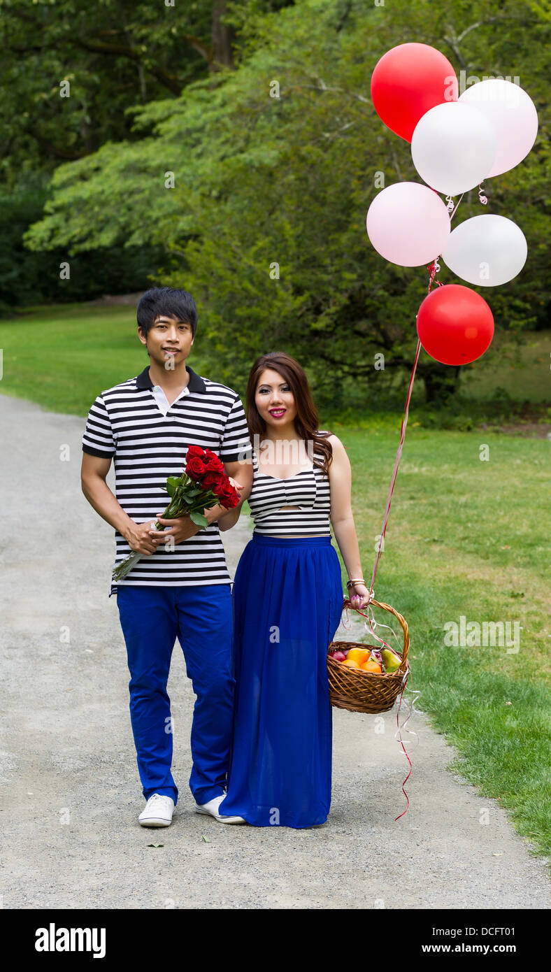 Photo verticale de young adult couple holding balloons, roses rouges et corbeille de fruits tandis que le sentier de randonnée pédestre Banque D'Images