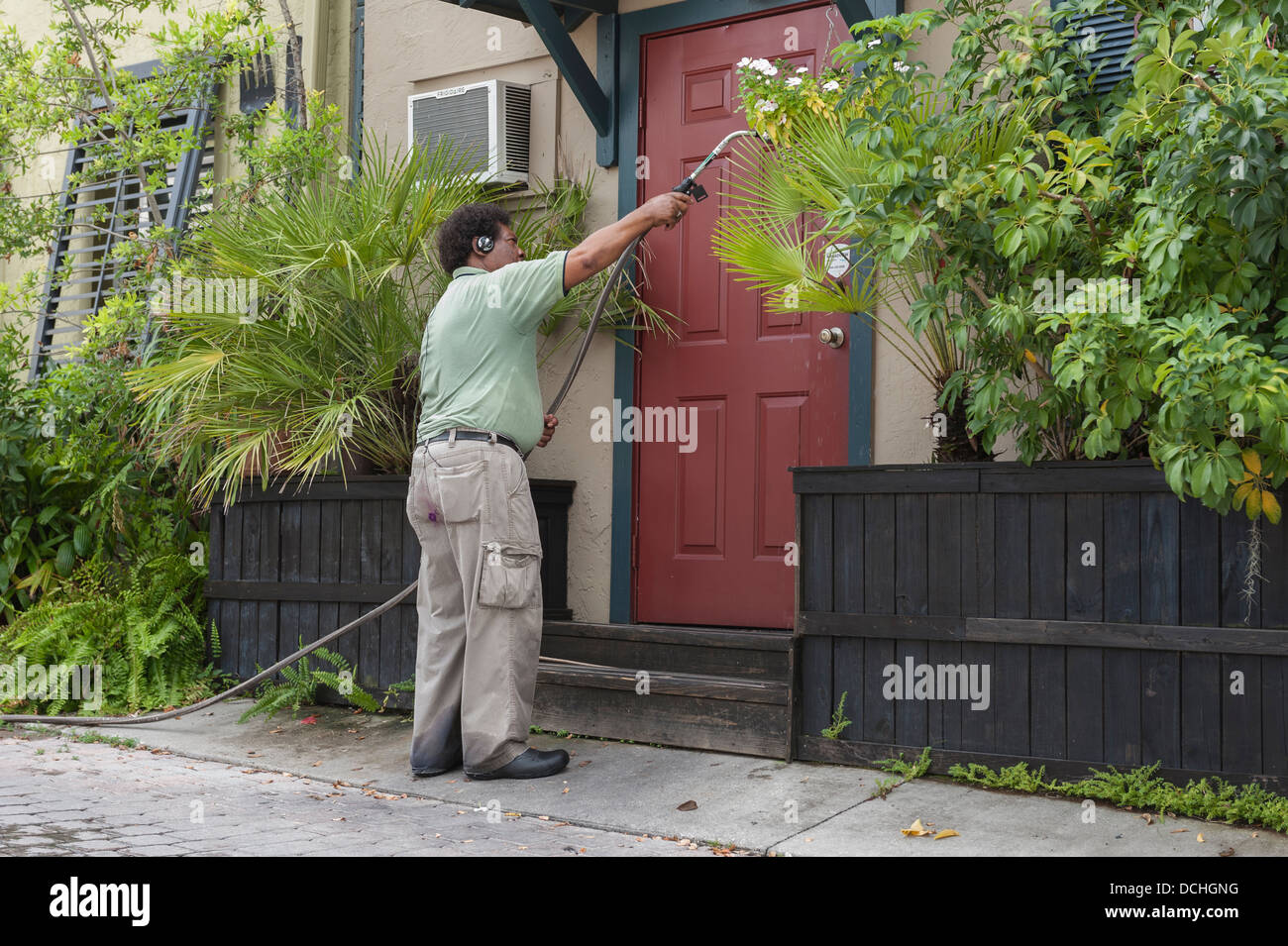 Un homme d'écouter de la musique sur son casque tandis que l'arrosage des plantes dans une ruelle de la ville de Mount Dora, Floride USA Banque D'Images