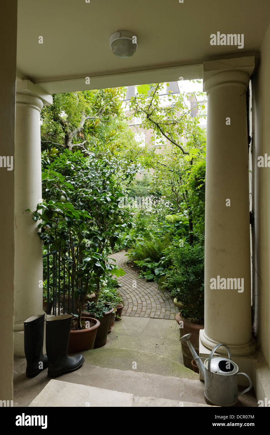 Portique à colonnes en pierre, arrosoir et bottes qui donnent sur le jardin luxuriant Banque D'Images