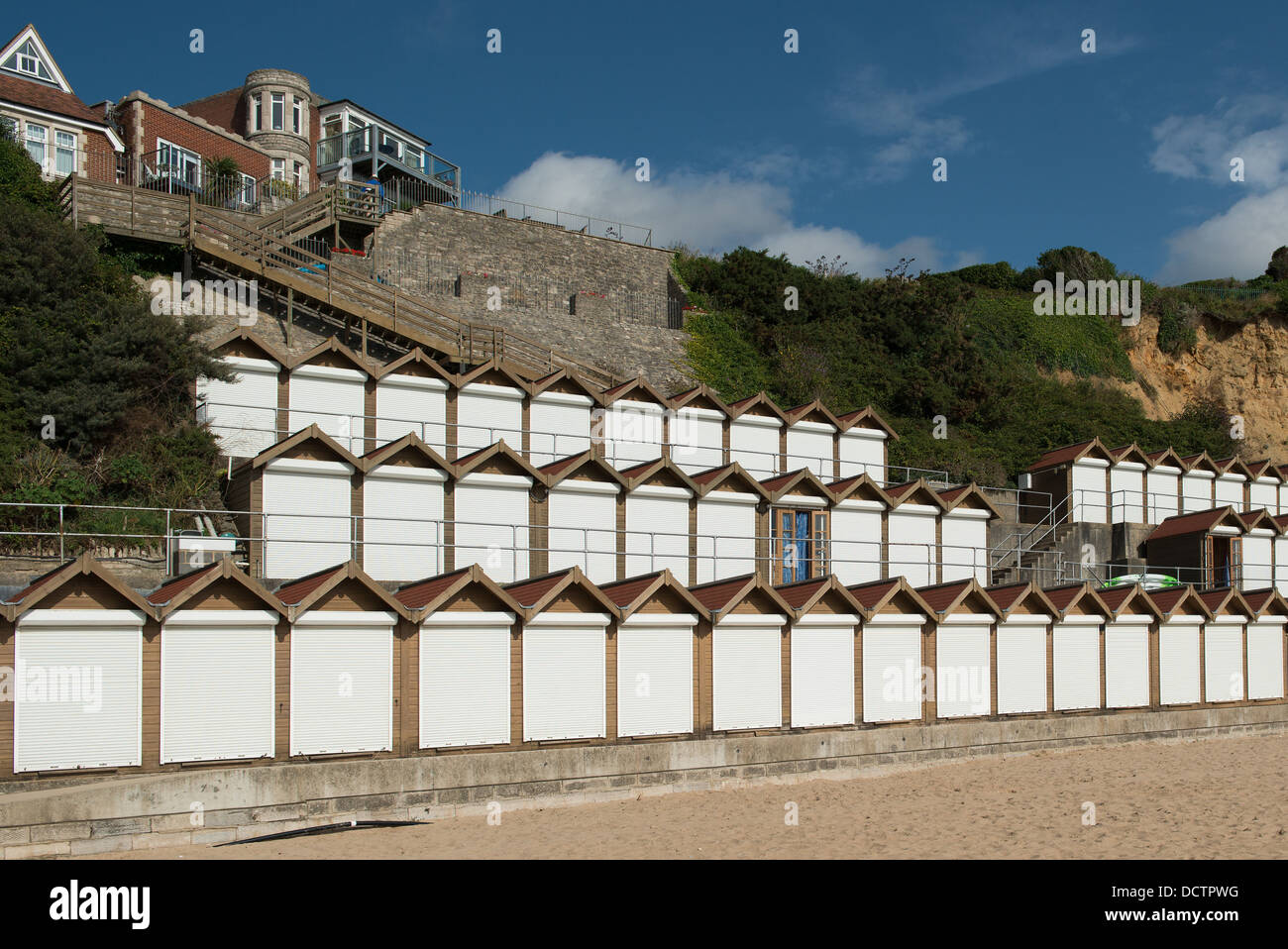 Trois rangées de porte dérobée blanc cabanes de plage à Swanage contre les falaises avec une porte ouverte et rideaux bleus sur la vue. Banque D'Images