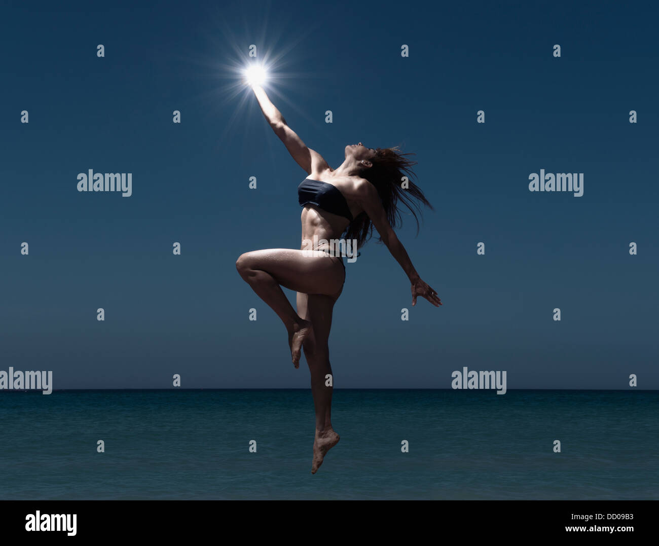 Une femme sautant au-dessus de l'eau tenant une lumière dans sa main ; Tarifa, Cadix, Andalousie, Espagne Banque D'Images