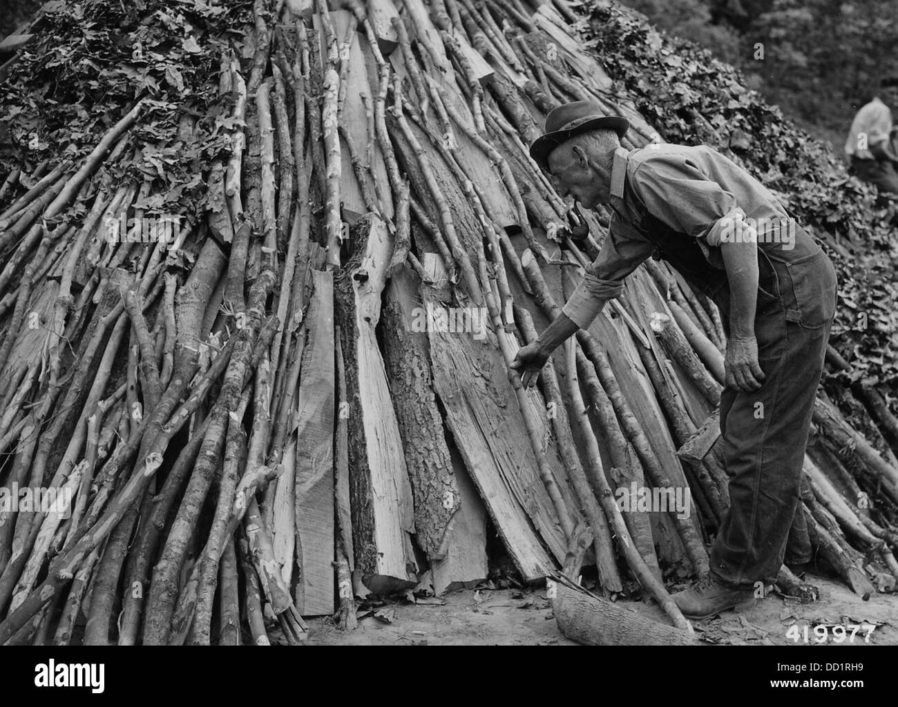 C.A. Masie est montré en train de préparer une nouvelle fosse de charbon de bois pour le charbon dans cette image. La production de charbon de bois était une partie essentielle des processus industriels au cours du XIXe et du début du XXe siècle, souvent utilisée dans les aciéries et la production d'acier. Banque D'Images