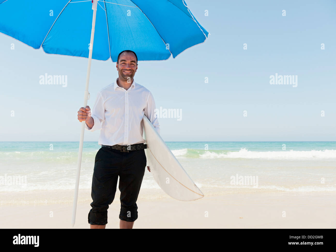 Un homme d'affaires sur la plage tenant un parapluie de plage et de surf ; Tarifa, Cadix, Andalousie, Espagne Banque D'Images