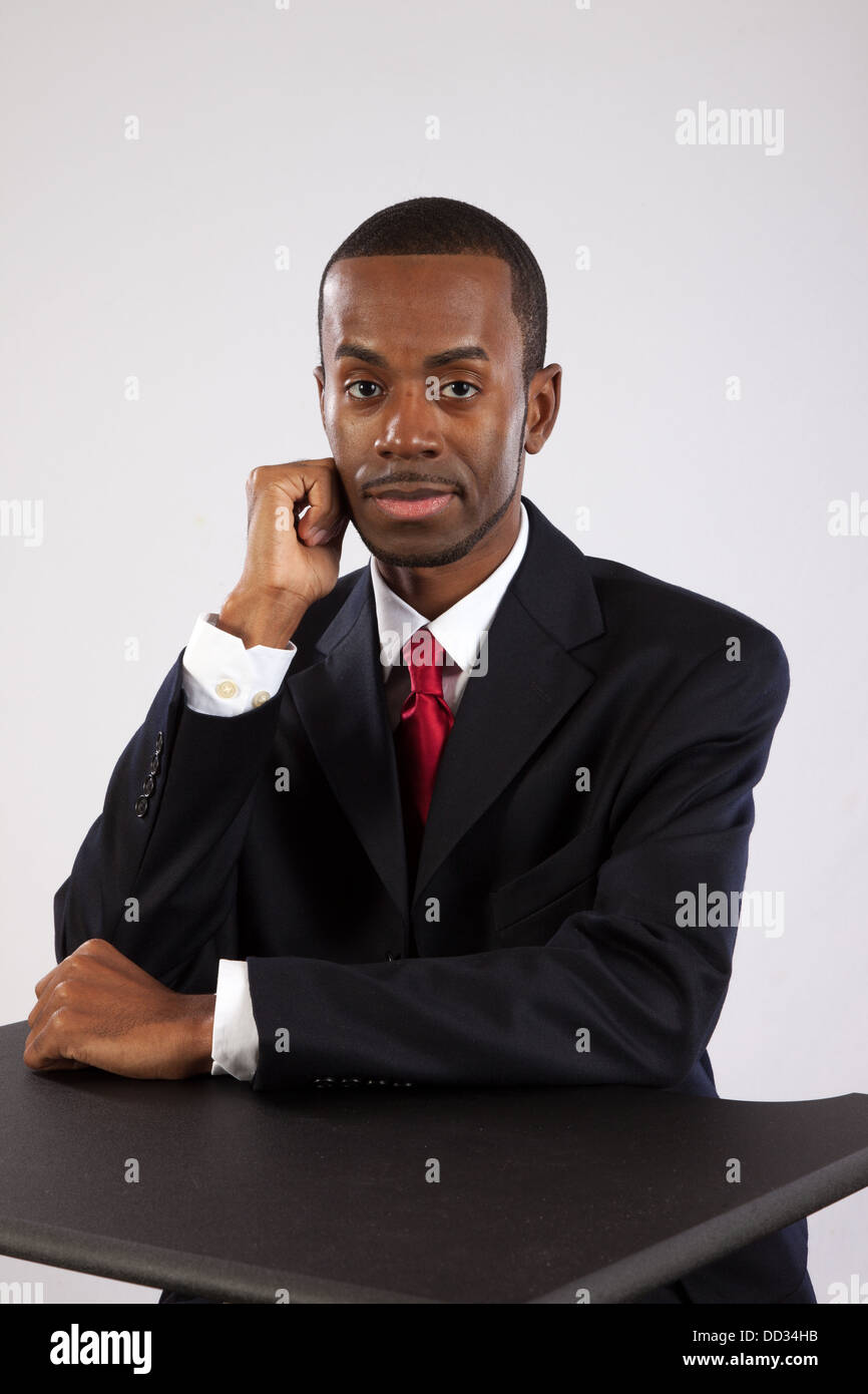 Beau black businessman dans un costume sombre et cravate rouge, assis avec  sa main sur son menton Photo Stock - Alamy