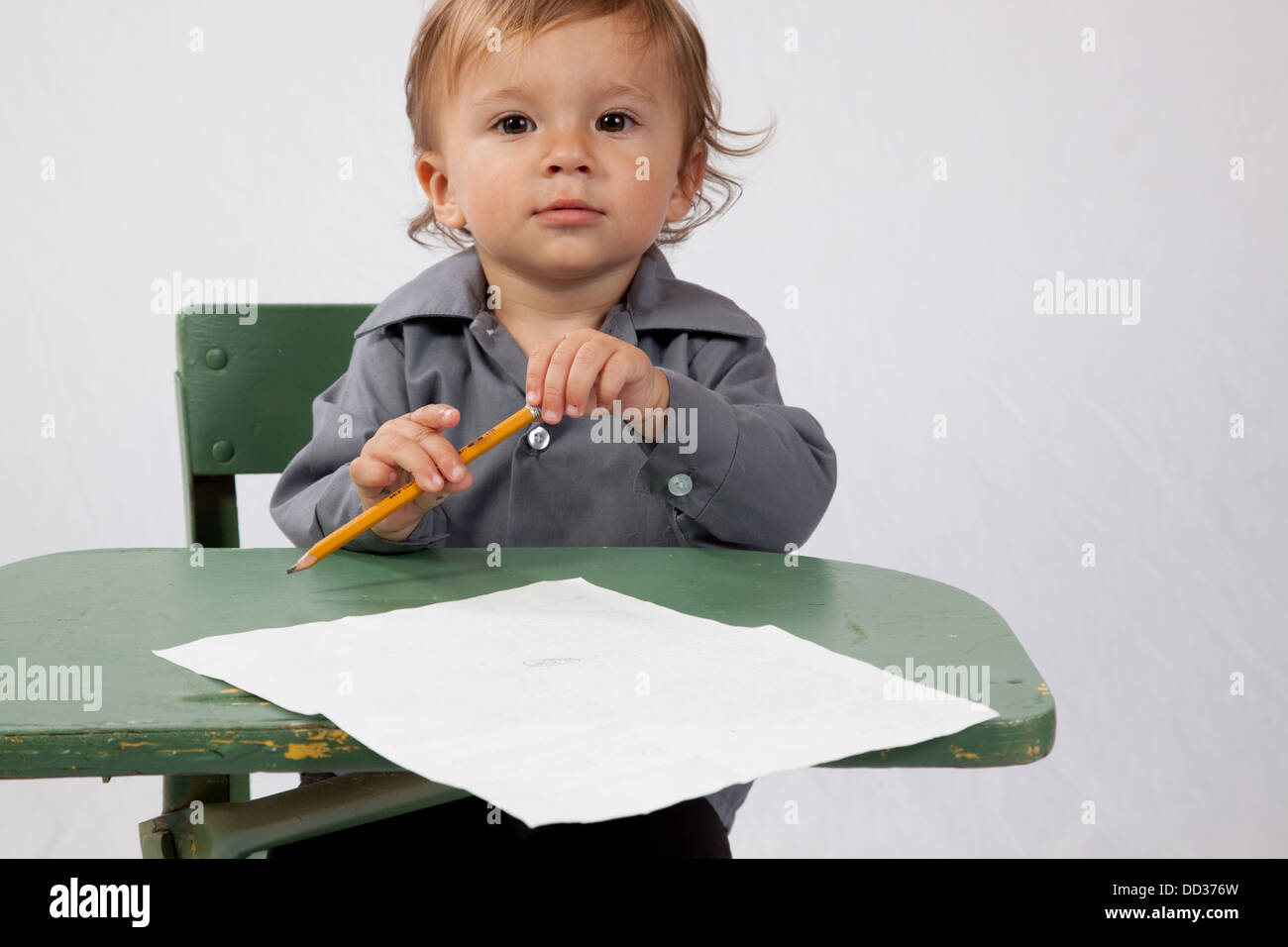 Jeune garçon assis à un bureau avec un morceau de papier et un crayon, à happy Banque D'Images