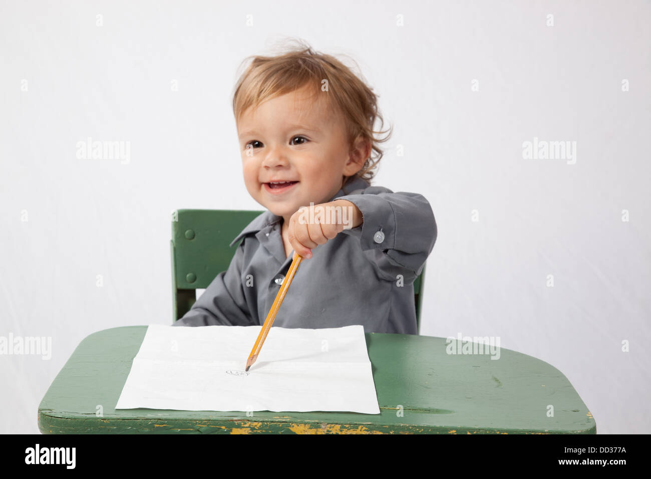 Jeune garçon assis à un bureau avec un morceau de papier et un crayon, à happy Banque D'Images