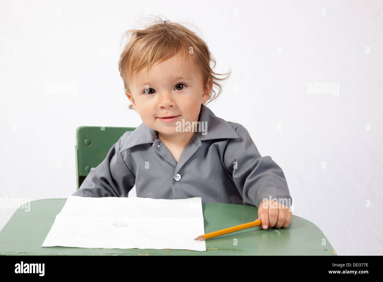 Jeune garçon assis à un bureau avec un morceau de papier et un crayon, à happy Banque D'Images