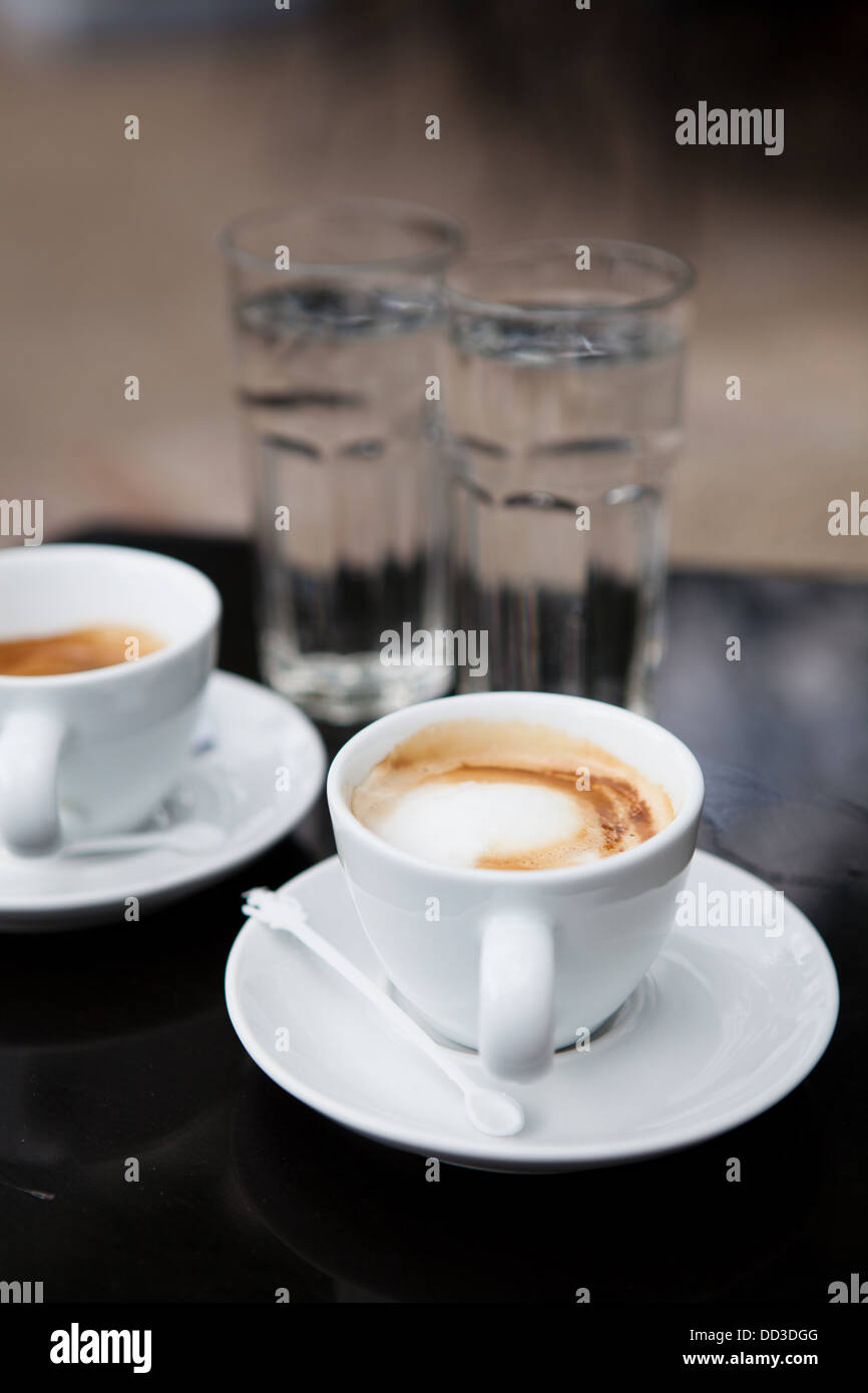 Deux cafés à base de lait en blanc tasses et verres d'eau sur cafe table Banque D'Images