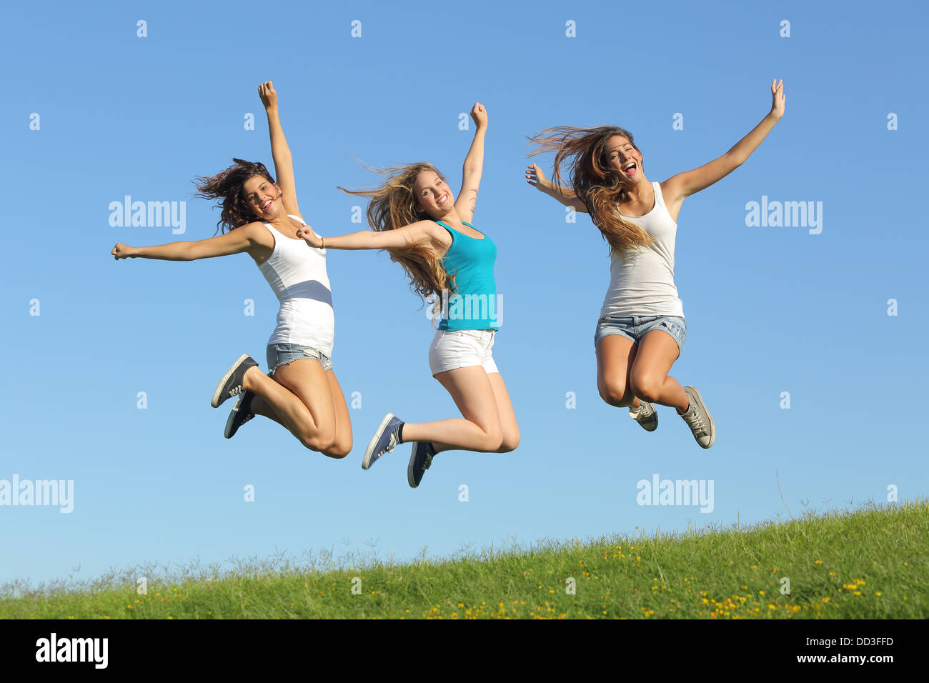 Groupe de trois adolescentes de sauter sur l'herbe avec le ciel bleu en arrière-plan Banque D'Images