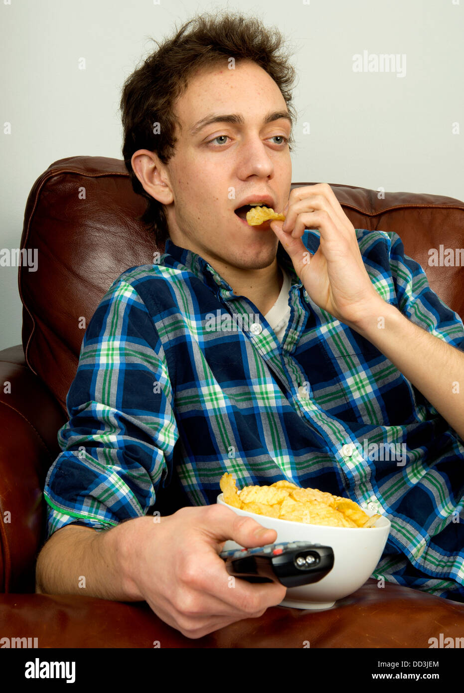 Jeune homme sur couch eating potato chips Banque D'Images